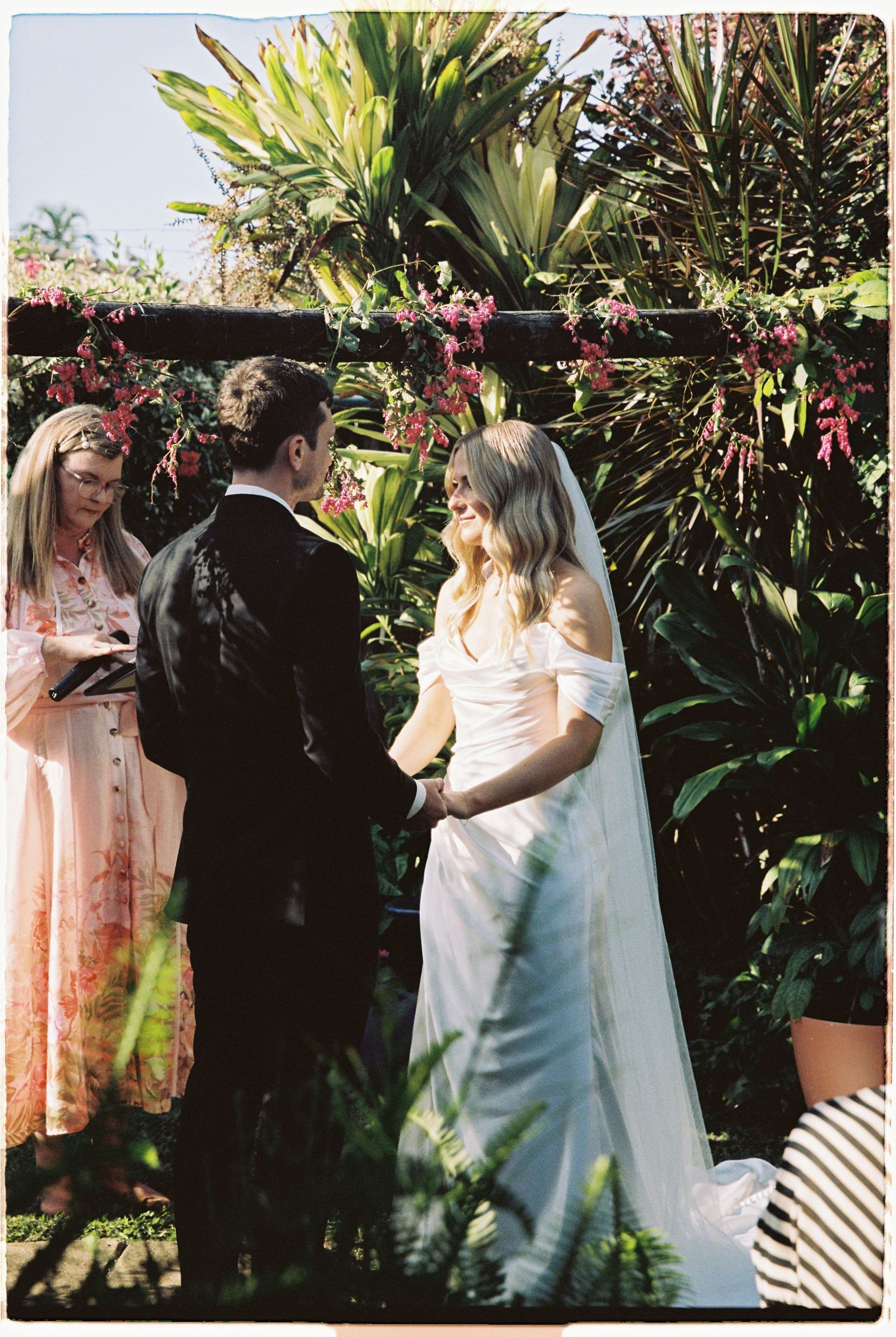 Bride and groom exchanging vows under floral arch with celebrant at garden wedding.