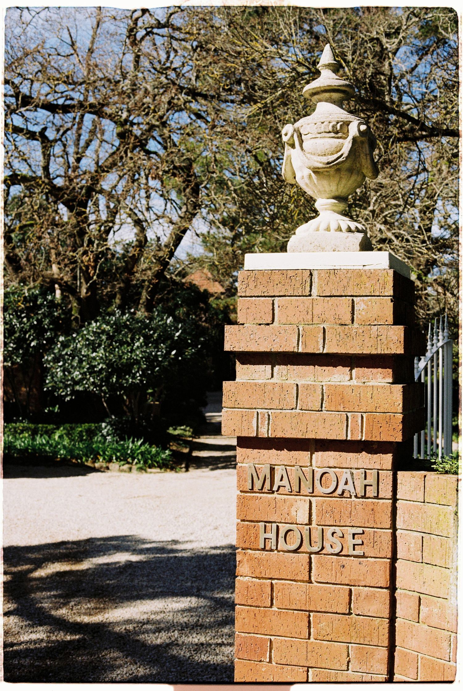 Brick gate pillar with decorative stone urn and Manoah House sign at venue entrance.