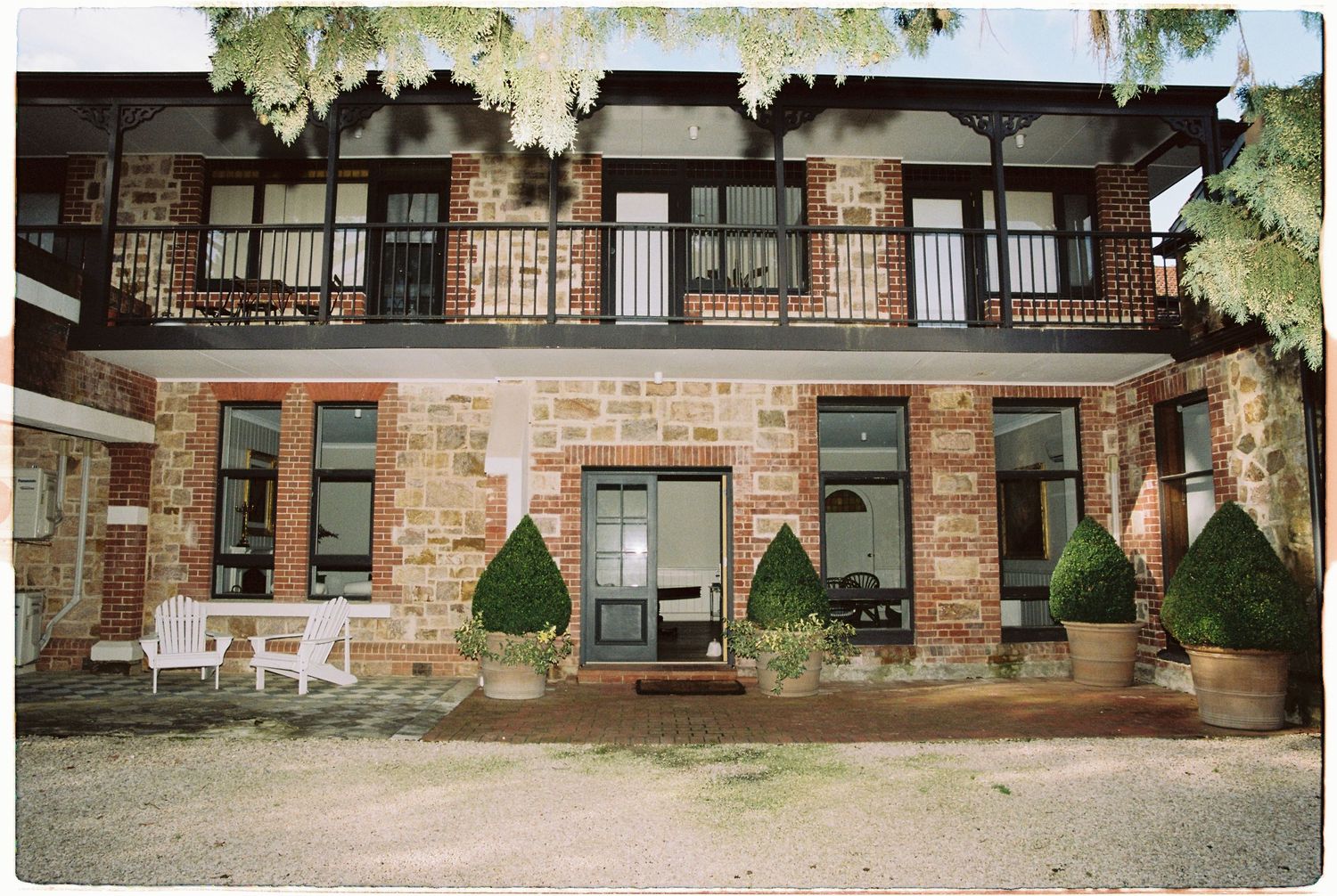 Rustic brick wedding venue with balconies, manicured hedges, and white outdoor furniture.