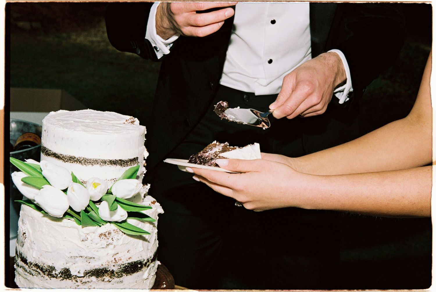Bride and groom cutting elegant white wedding cake decorated with white tulips at reception.