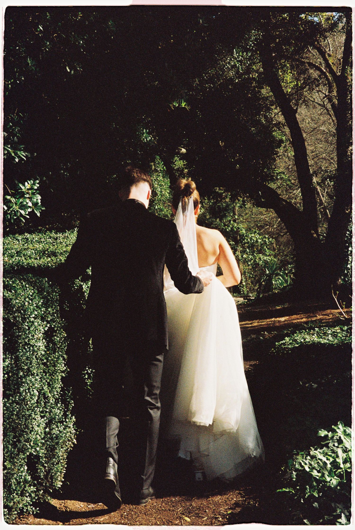 Bride and groom walking hand in hand through a lush garden path on their wedding day.