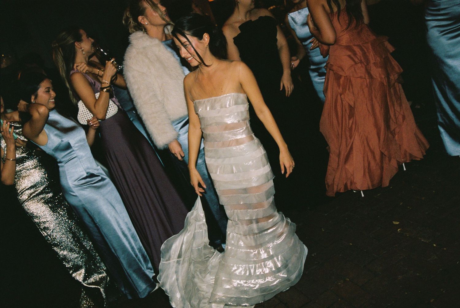 A woman in a layered strapless gown dances among guests at a formal event.