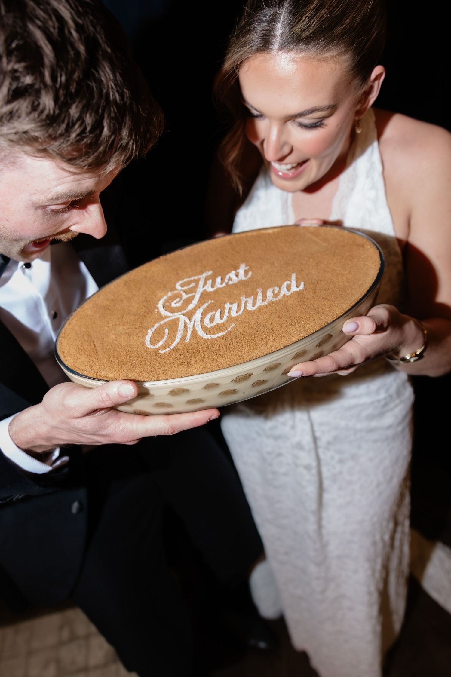 Newlyweds holding a decorative Just Married keepsake dish, bride in white gown and groom in tuxedo smiling together.