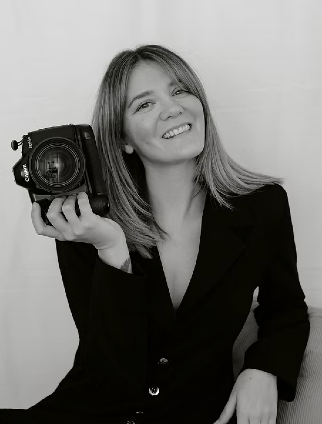 Black and white portrait of a smiling woman holding a camera, wearing a black blazer, perfect for photography brand.