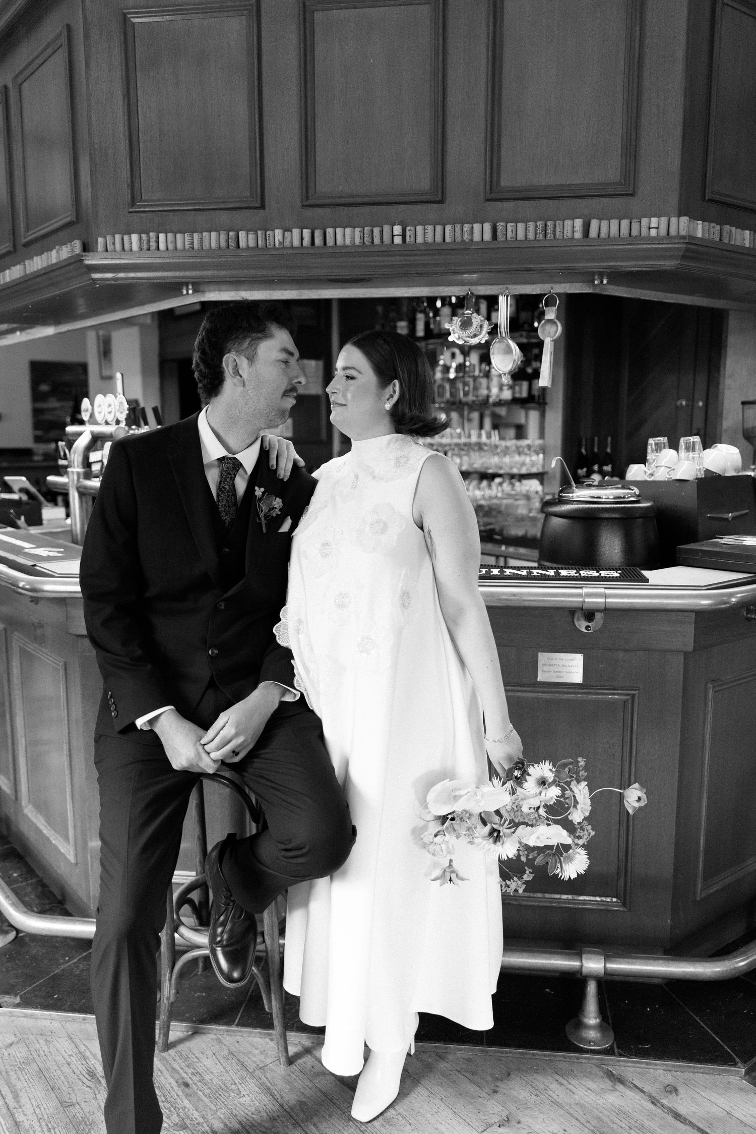 Black and white photo of a bride and groom sharing a romantic moment at a bar, bride holding a bouquet.