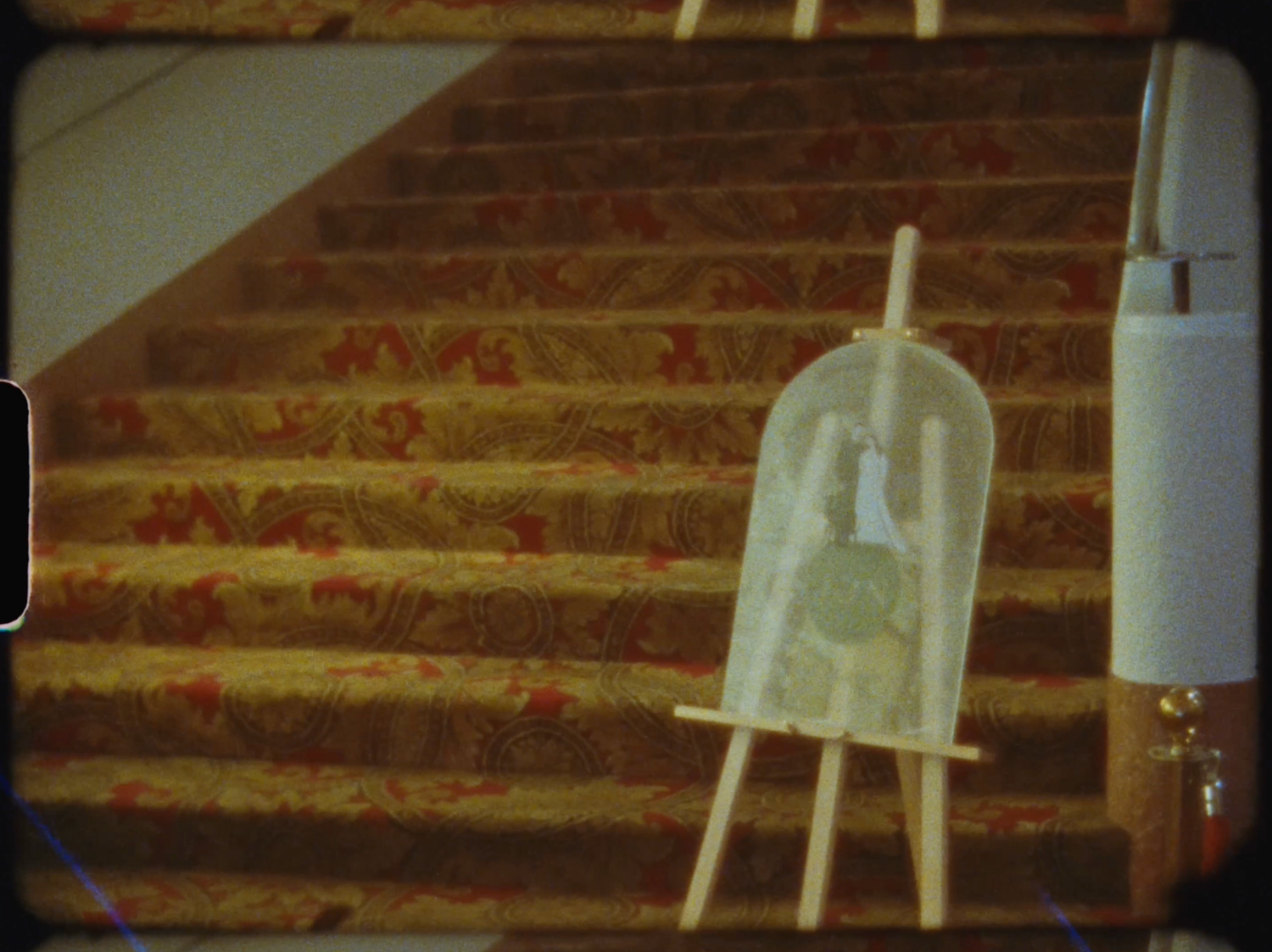 Wooden easel displaying a framed artwork on patterned staircase steps with red floral carpet design.