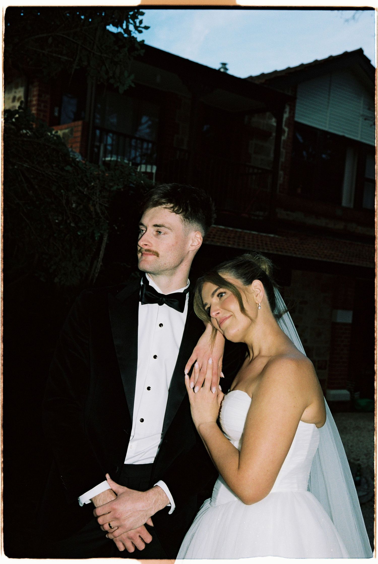 Bride leaning on grooms shoulder in wedding attire during golden hour portrait.