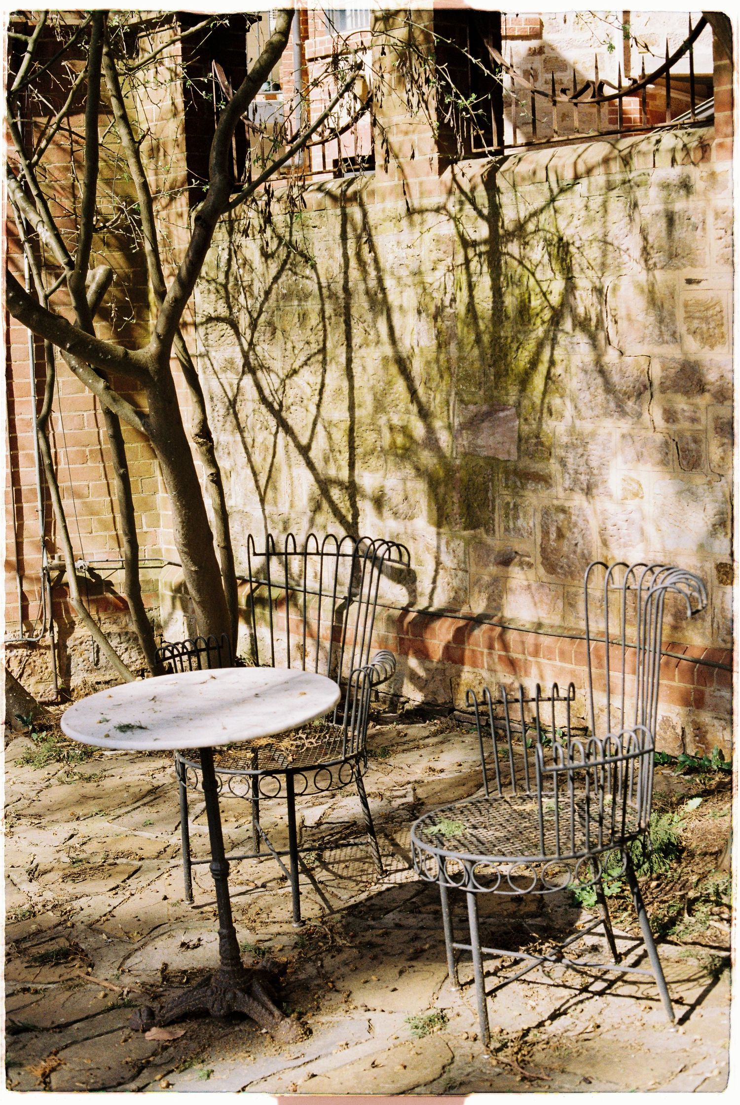 Vintage wrought iron table and chairs in a sunlit courtyard beside a stone wall.