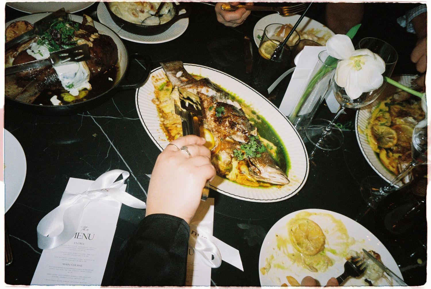 Elegant whole roasted fish dish served on white platter at wedding reception dinner table with floral decorations.