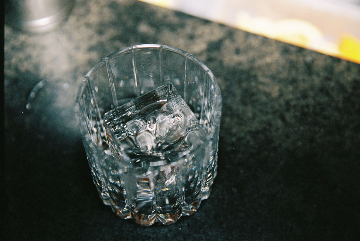 Crystal rocks glass filled with ice on a dark granite bar counter.