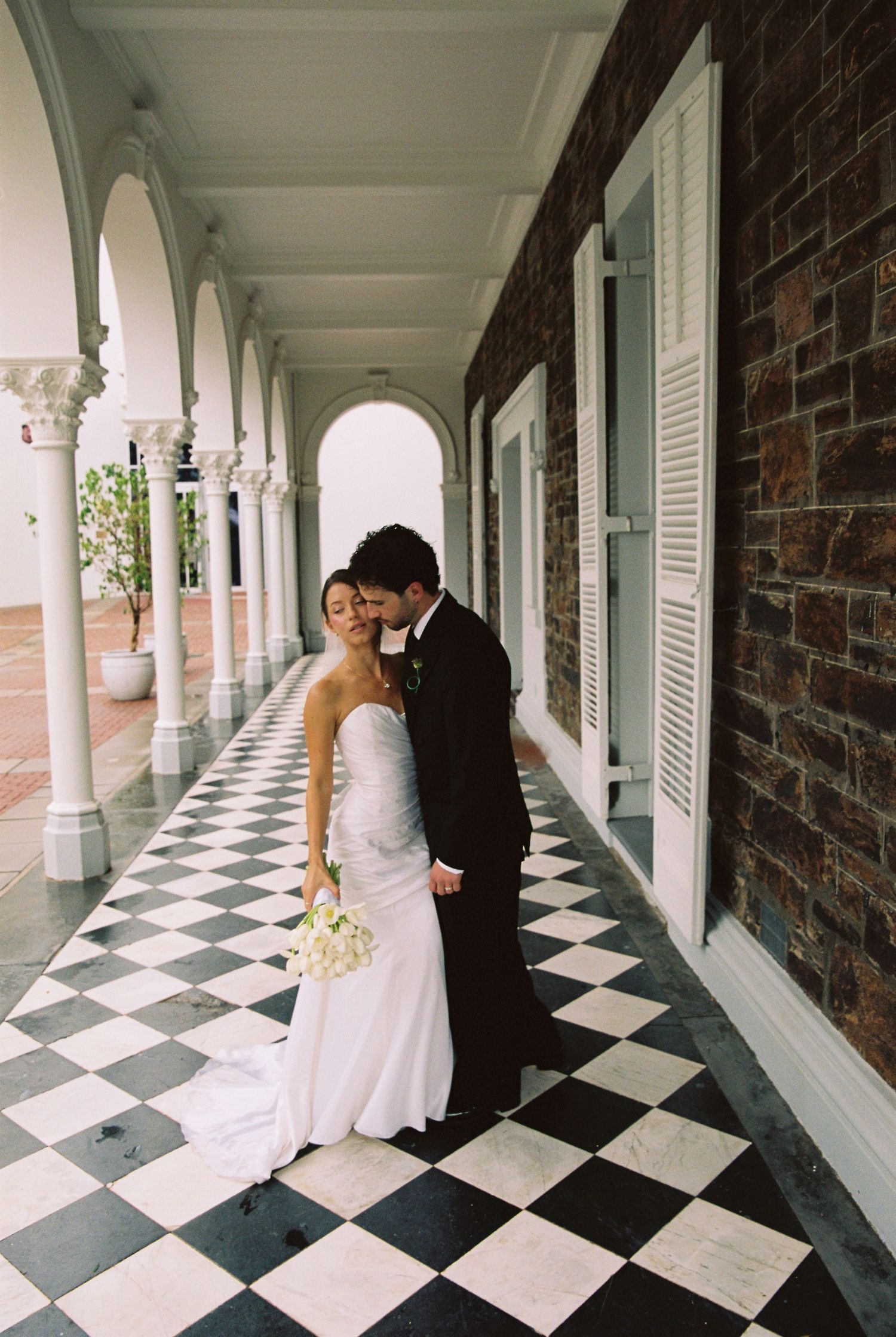 Bride and groom sharing a romantic moment on a checkered floor colonnade at their elegant wedding venue.