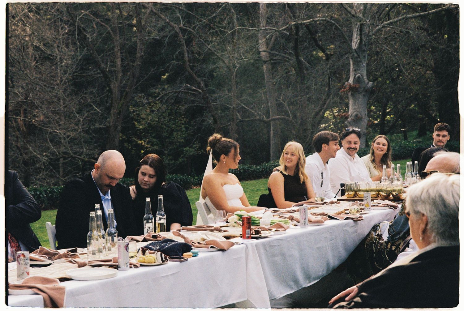 Wedding guests enjoy an outdoor reception dinner at a long elegantly set table.