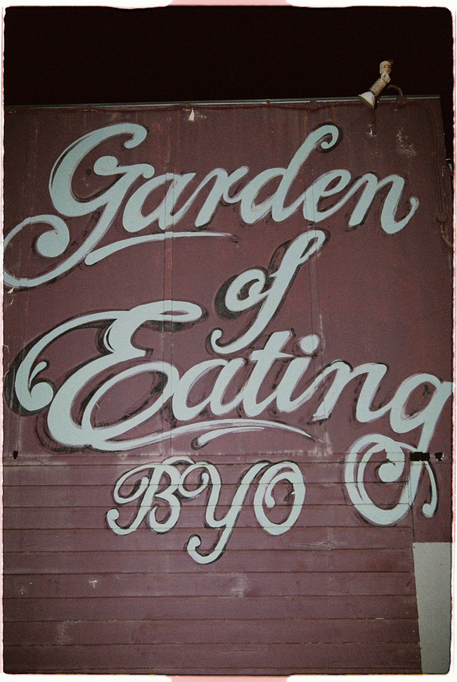 Vintage hand-painted sign reading Garden of Eating BYO on a dark red wall.