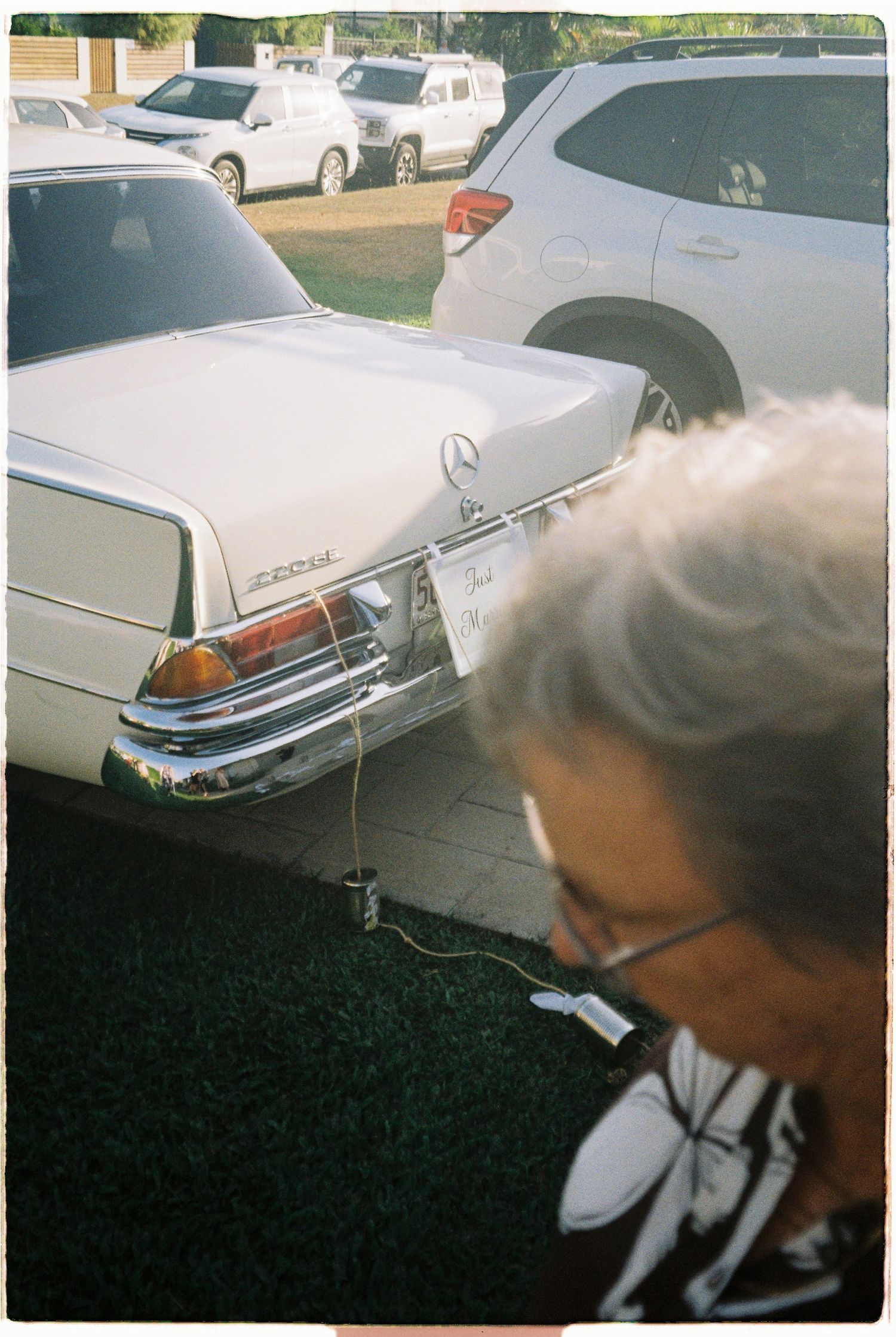 Elderly guest stands near vintage white Mercedes Just Married wedding car.