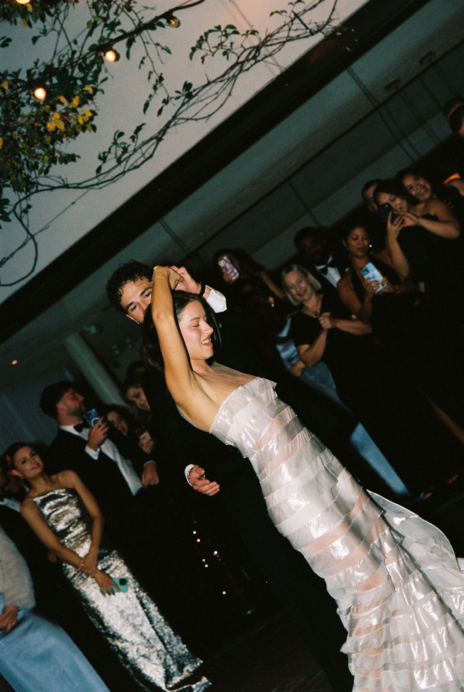 Bride in ruffled white gown twirls during first dance at elegant wedding reception with guests watching.