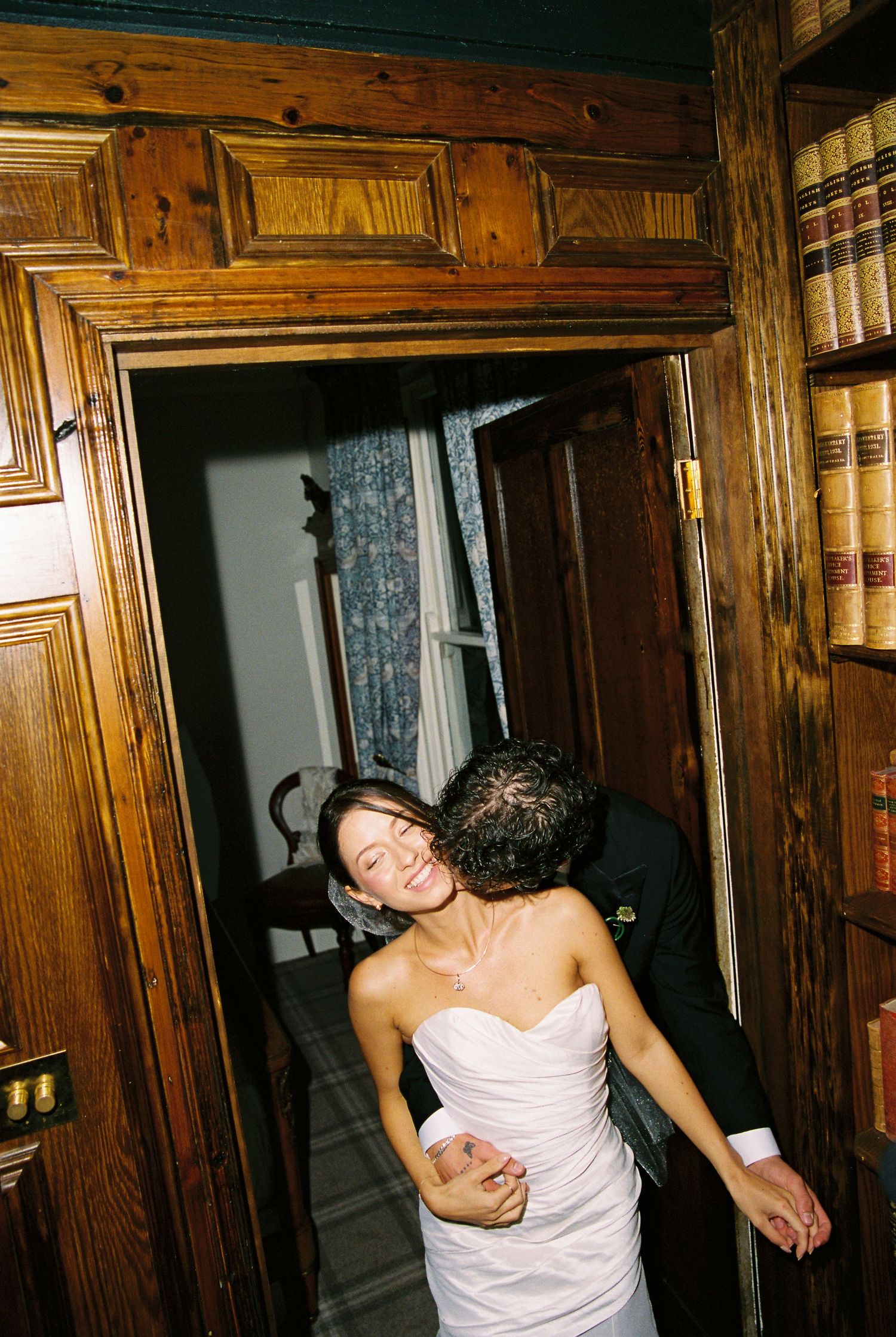 Bride in strapless white gown embracing groom in black suit in a wooden doorway.