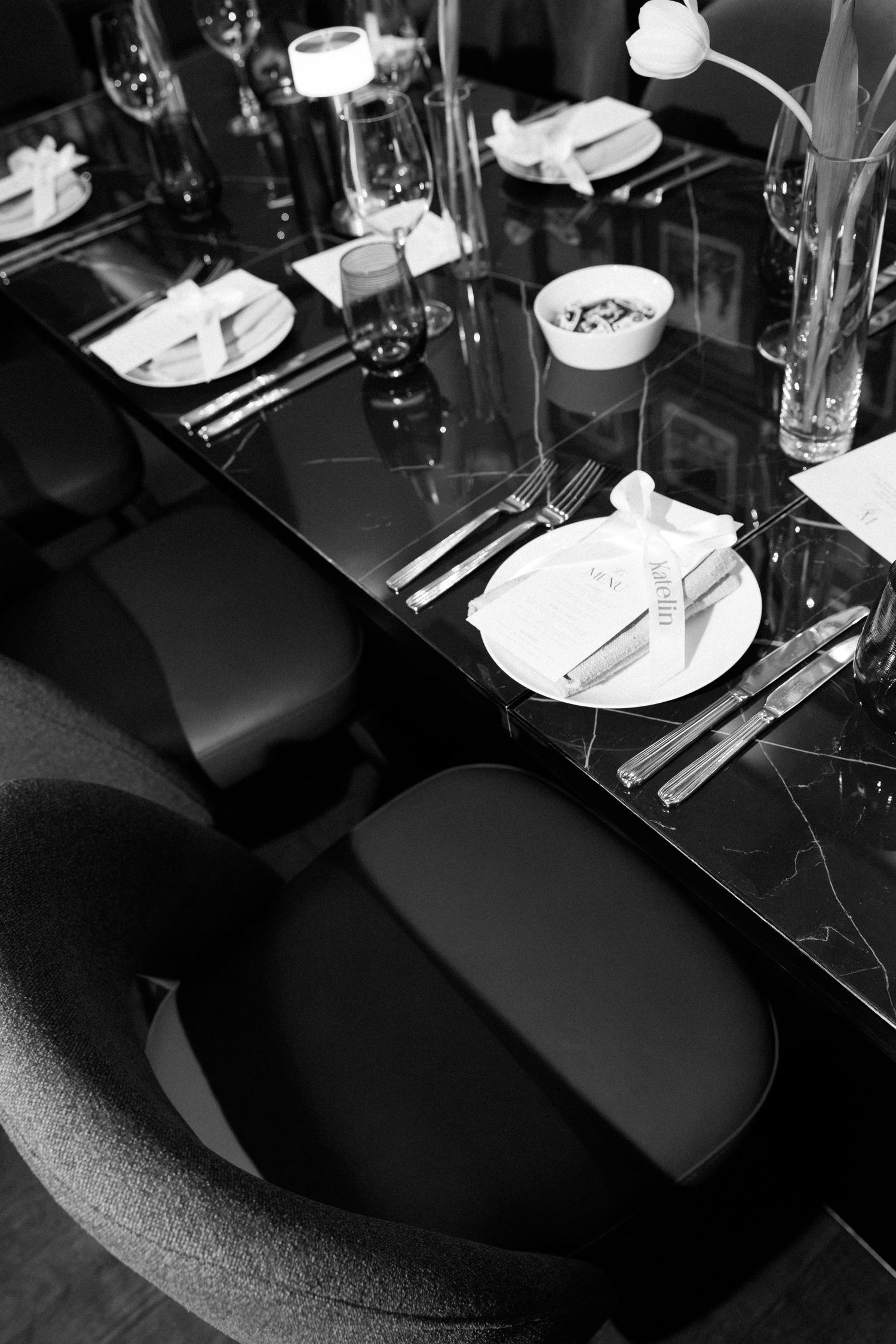 Black and white photo of an elegant restaurant table setting with marble surface, white plates, silverware, and modern chairs.