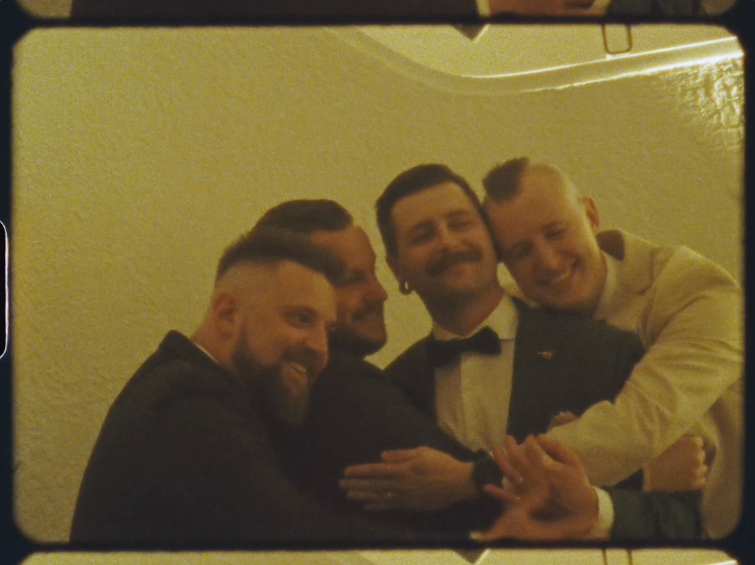 Four men in formal attire smile and pose together at a celebration.