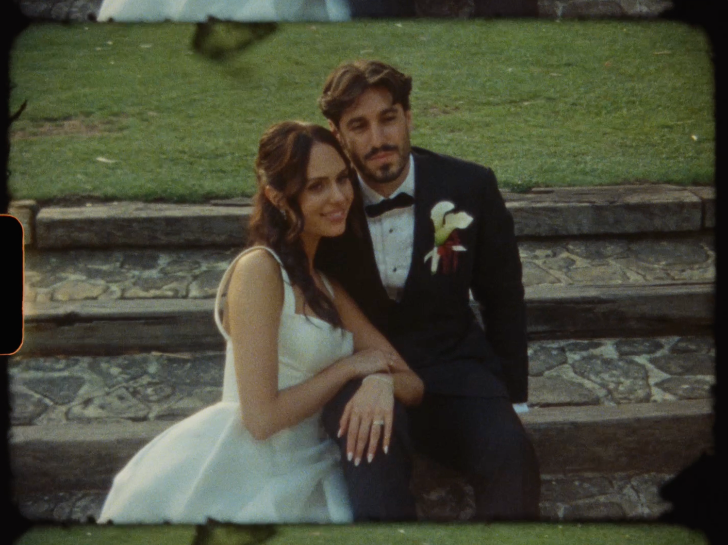 Bride and groom sit closely together on stone steps, smiling for a romantic wedding portrait outdoors.