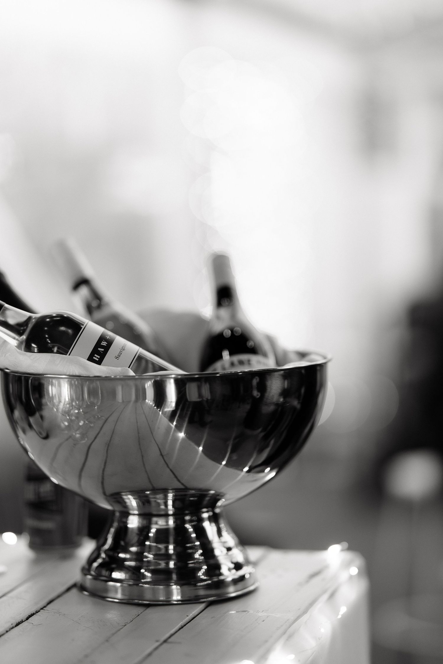 Black and white photo of wine bottles chilling in a polished silver ice bucket on a wooden table.