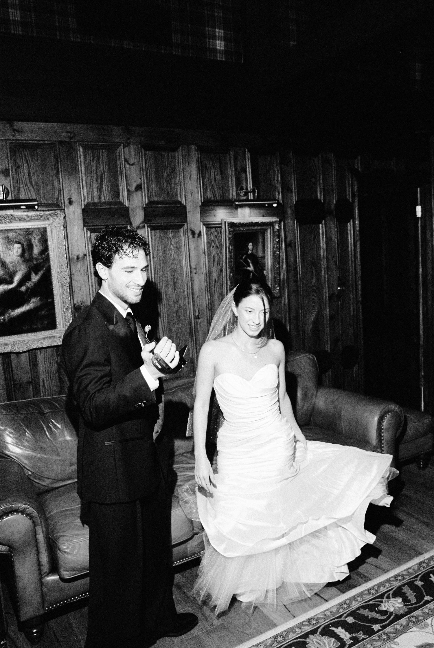 Bride and groom sharing a moment in a dark wood-paneled reception room.