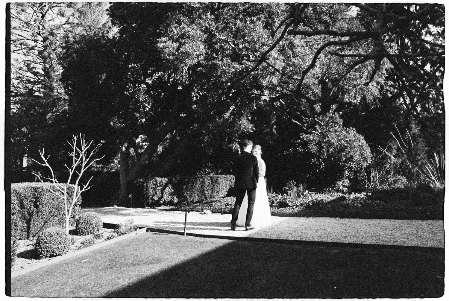 Black and white photo of bride and groom embracing in a lush garden setting.