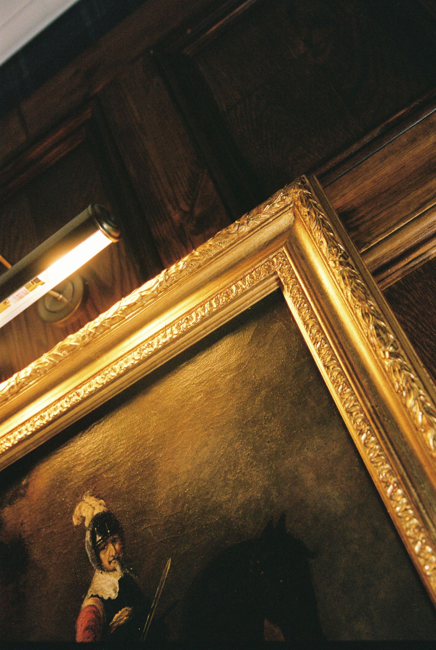 Close-up of ornate gold-framed oil painting on dark wood-paneled wall.