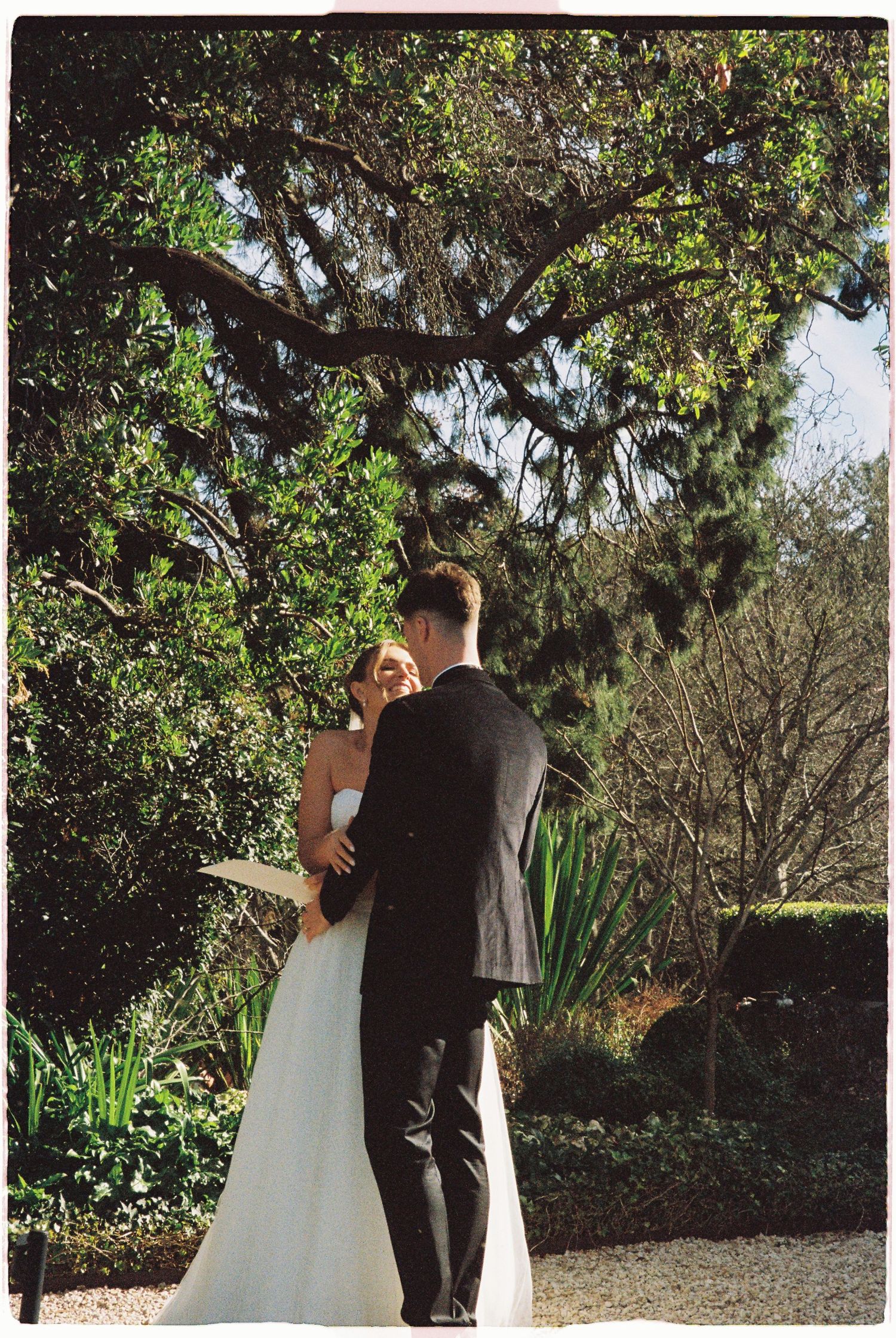 Bride and groom share an intimate moment under a large tree during outdoor wedding ceremony.