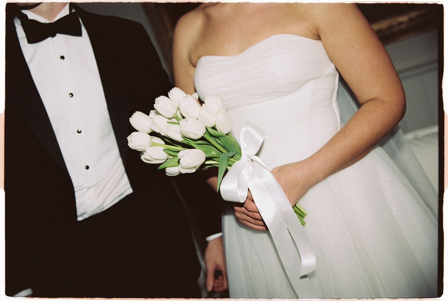 Bride holds elegant white tulip bouquet tied with ribbon beside groom.