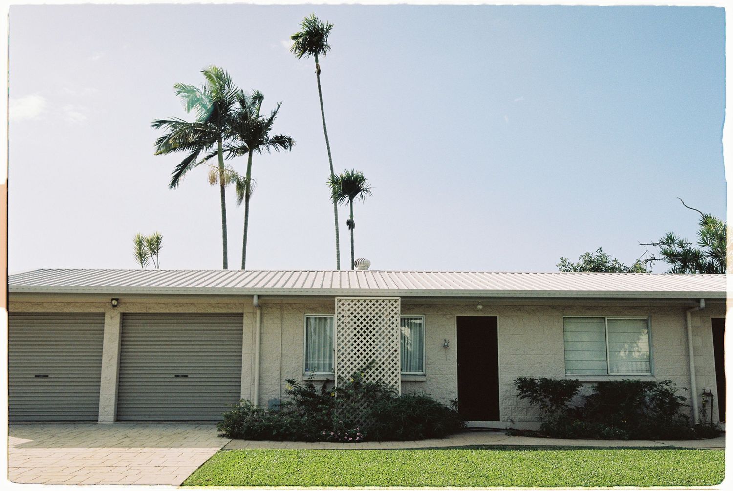 Single-story Florida home with white roof, two-car garage, and tall palm trees against blue sky.