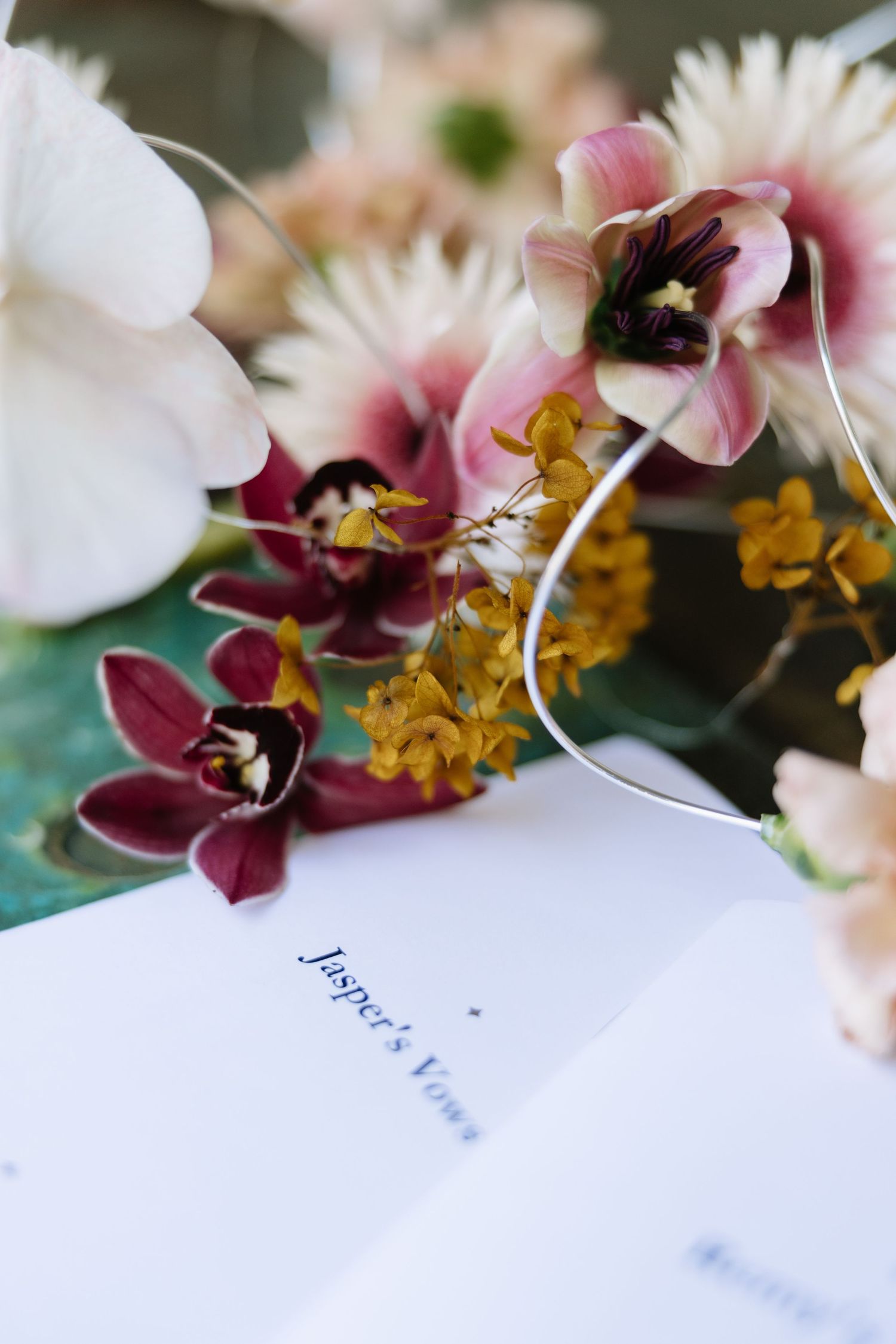 Wedding vows card named Jasper's surrounded by elegant orchids and wildflowers in pink, burgundy, and yellow tones.