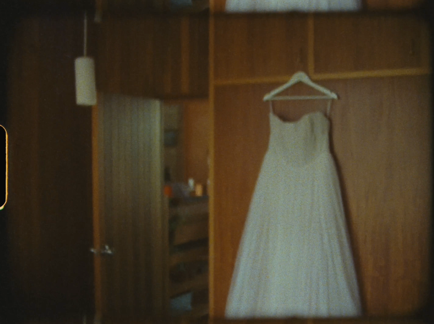 Elegant white strapless wedding dress hanging on wooden wardrobe in a room.