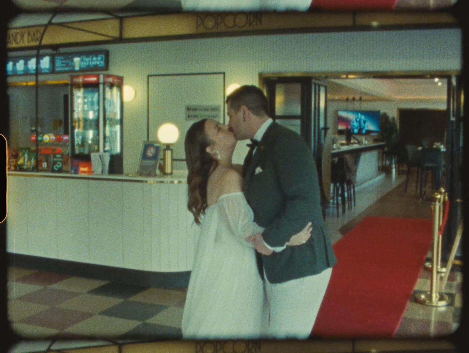 A bride and groom share a romantic kiss in a elegant venue lobby with red carpet.