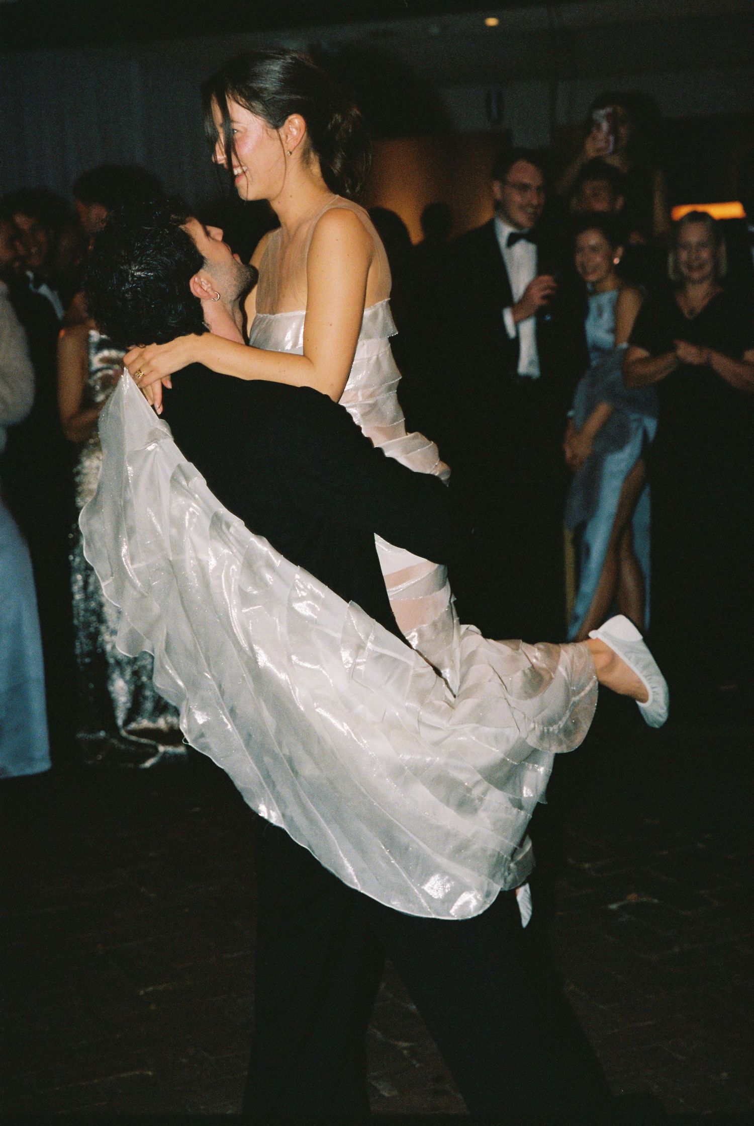 Groom lifting bride in white ruffled gown during first dance at wedding reception.