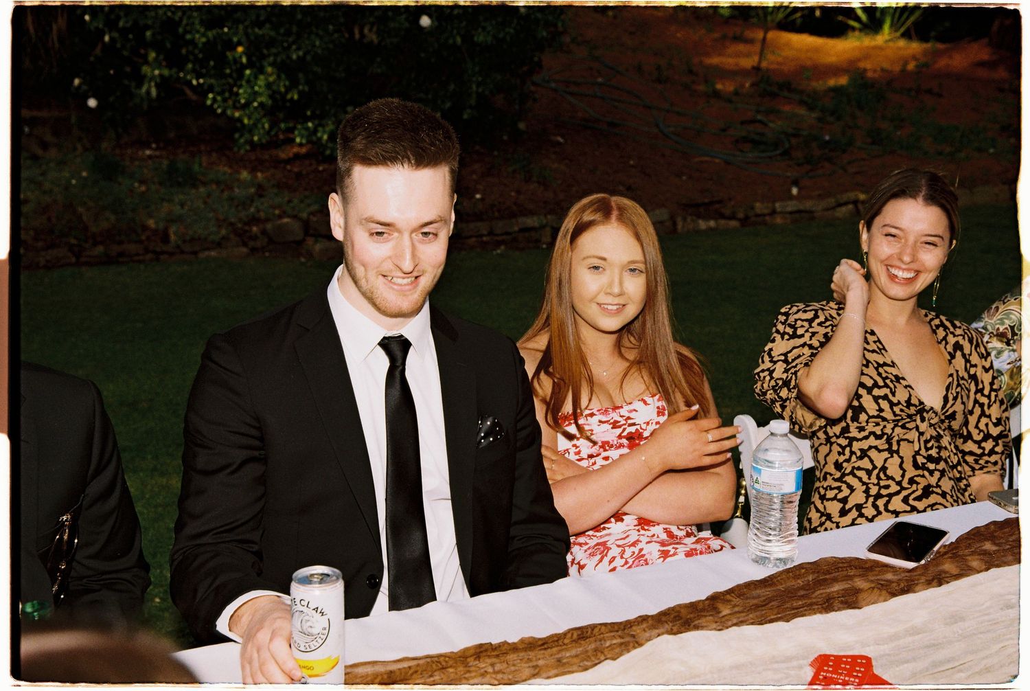 Three wedding guests smiling at outdoor reception dinner table at night.