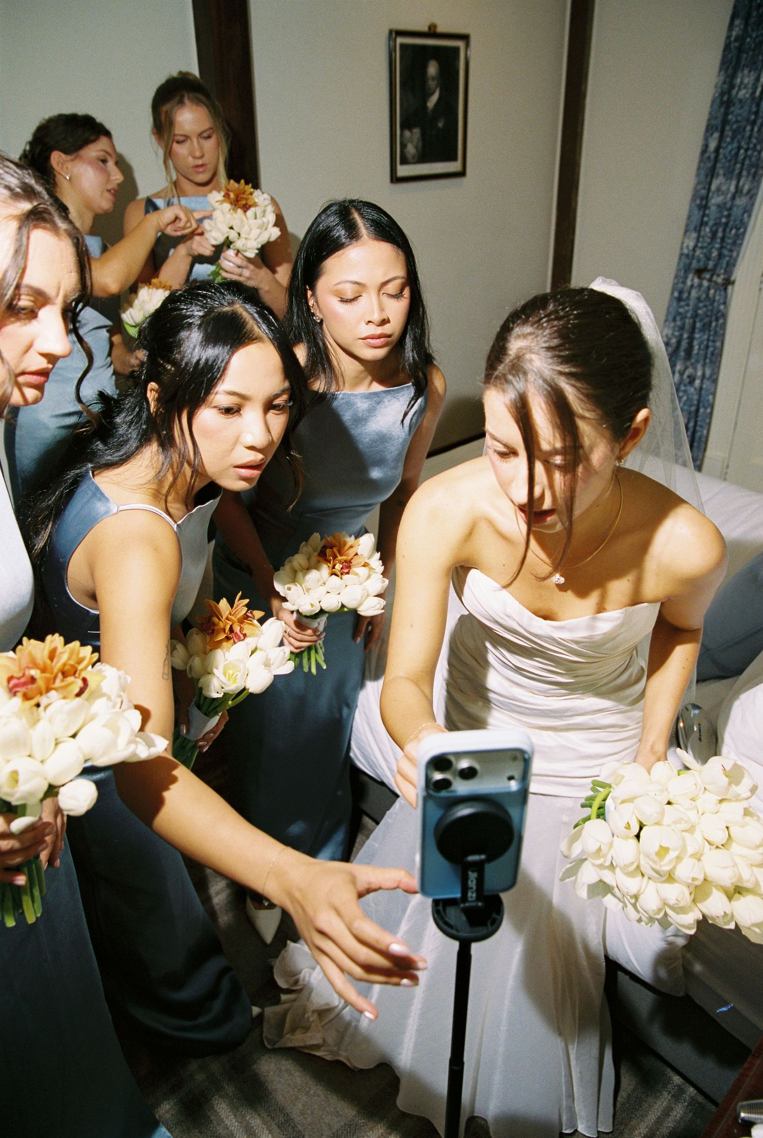 Bride in strapless gown and bridesmaids in blue satin dresses checking phone before ceremony.