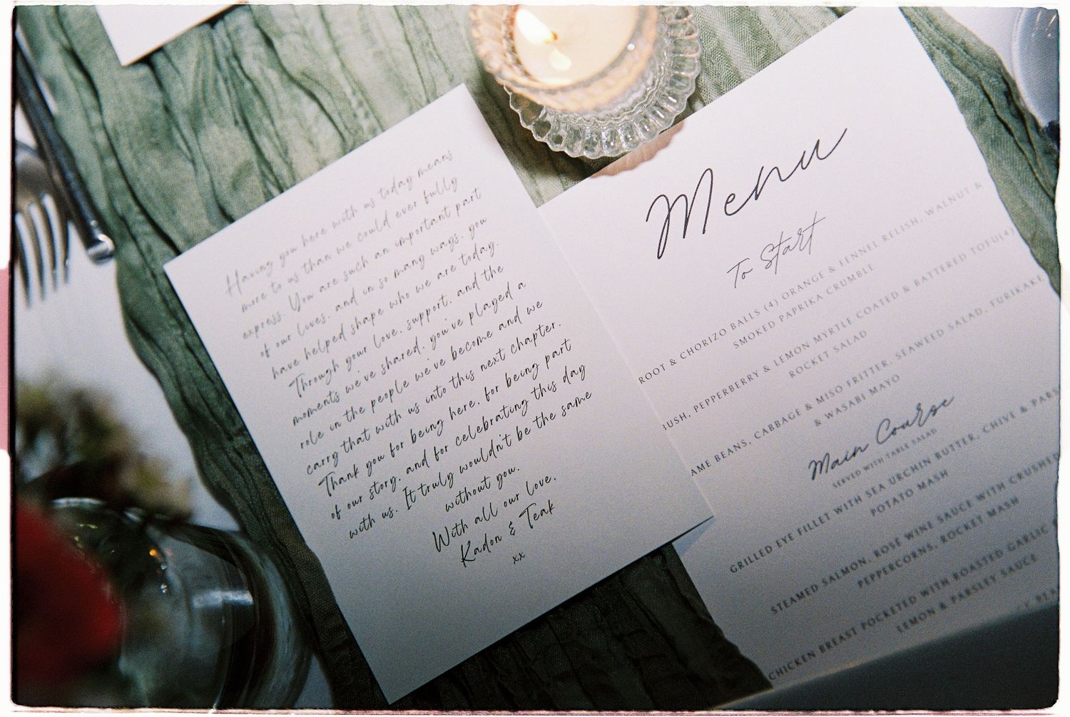 Elegant wedding menu card and handwritten letter displayed on rustic wooden table with candlelight.