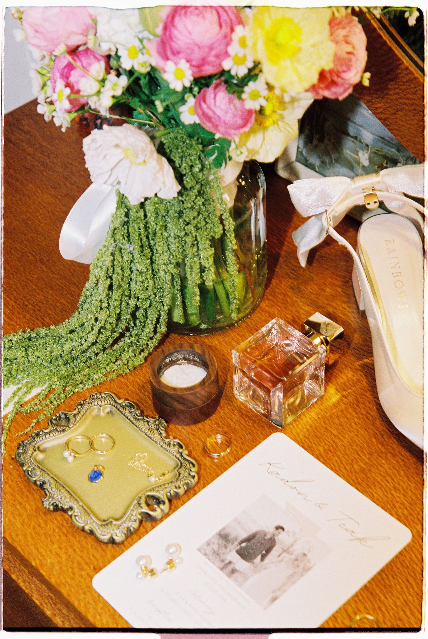 Wedding flat lay with colorful floral bouquet, rings, perfume bottle, bridal shoes, and invitation.