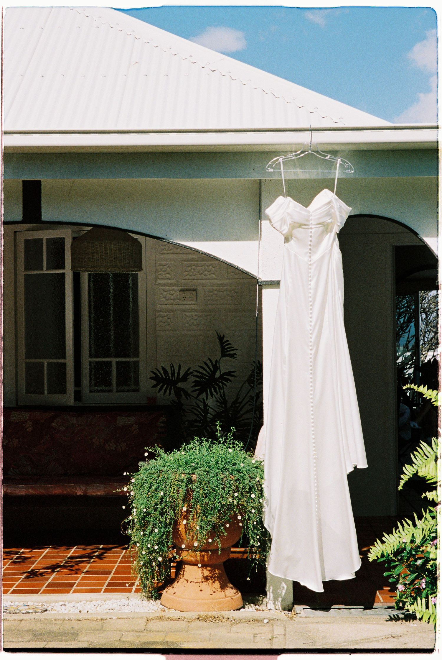 Elegant white bridal gown hanging outside a charming cottage home on a sunny day.