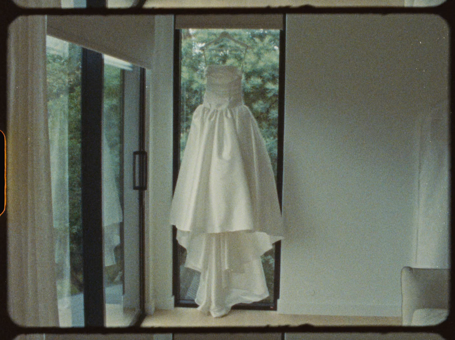 Elegant white wedding dress hanging in a doorway with natural garden light behind it.