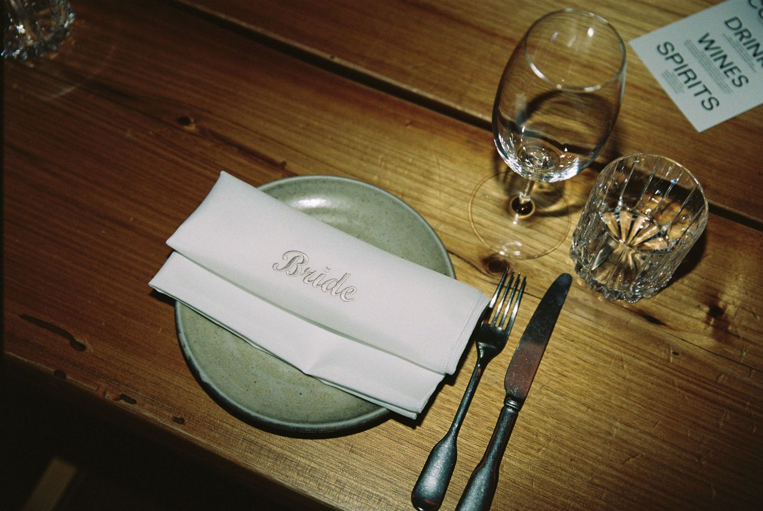 Wedding place setting with bride nameplate napkin on sage plate with crystal glassware on wood table.