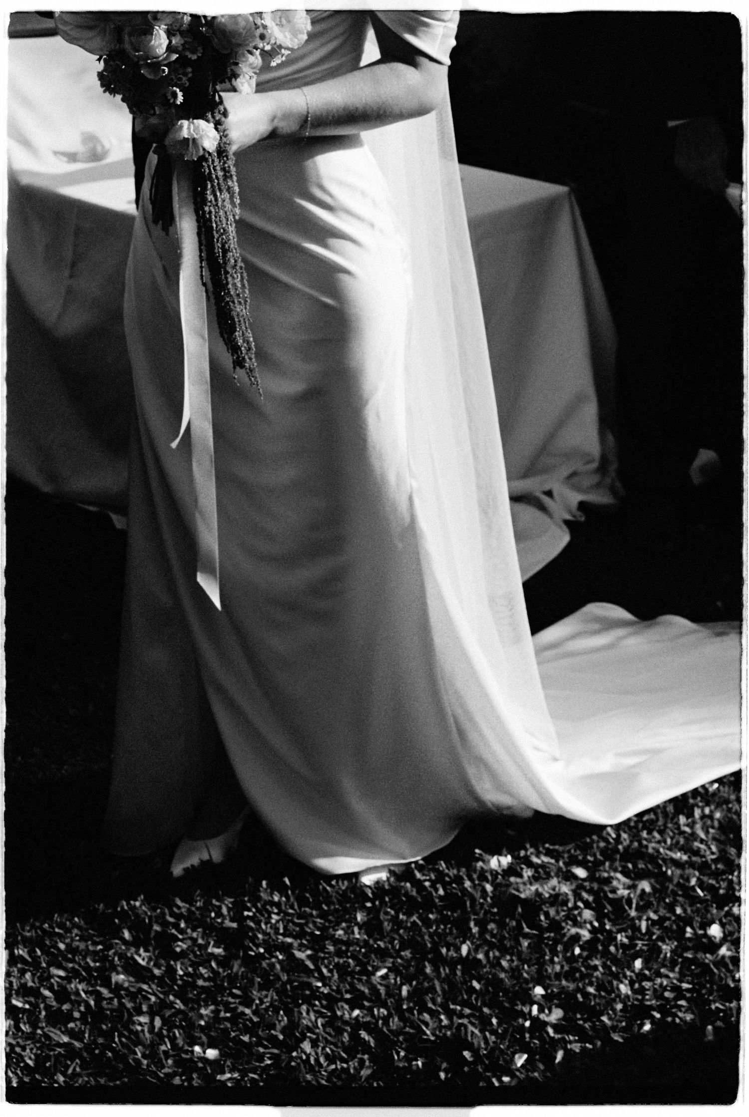 Black and white photo of a bride in a flowing white wedding dress holding a bouquet outdoors.
