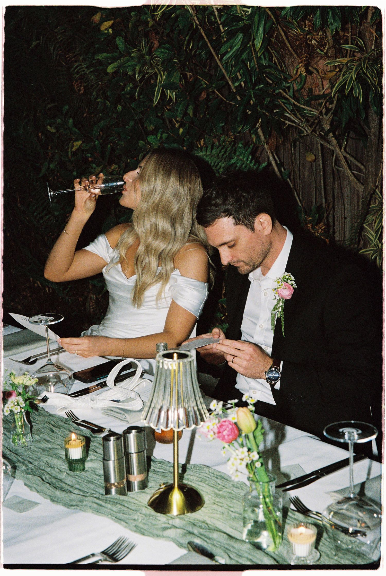 Bride and groom seated at elegantly decorated marble reception table with candles and floral arrangements.