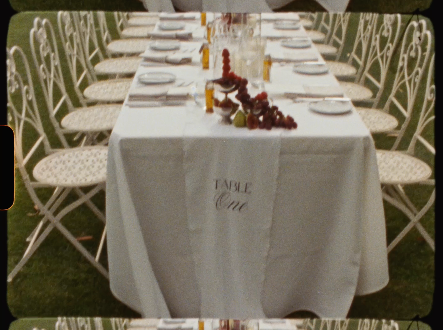 Elegantly set outdoor wedding reception table with white linen labeled Table One and floral centerpieces.