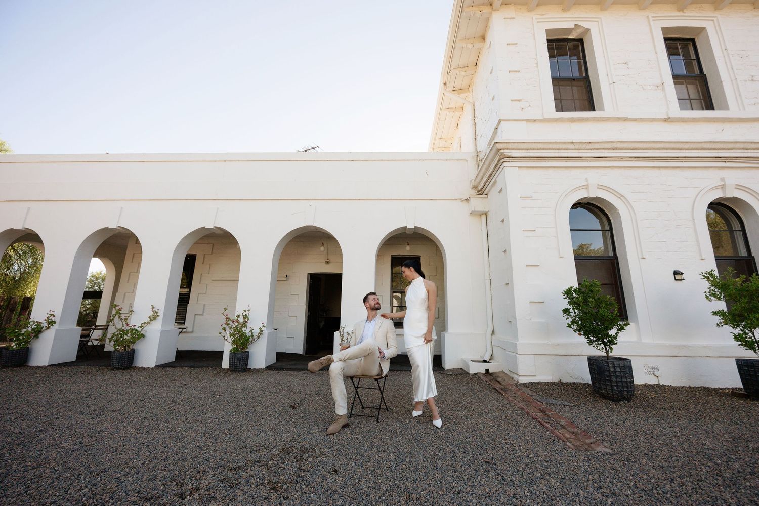 Bride and groom share a playful moment outside elegant white arched wedding venue.
