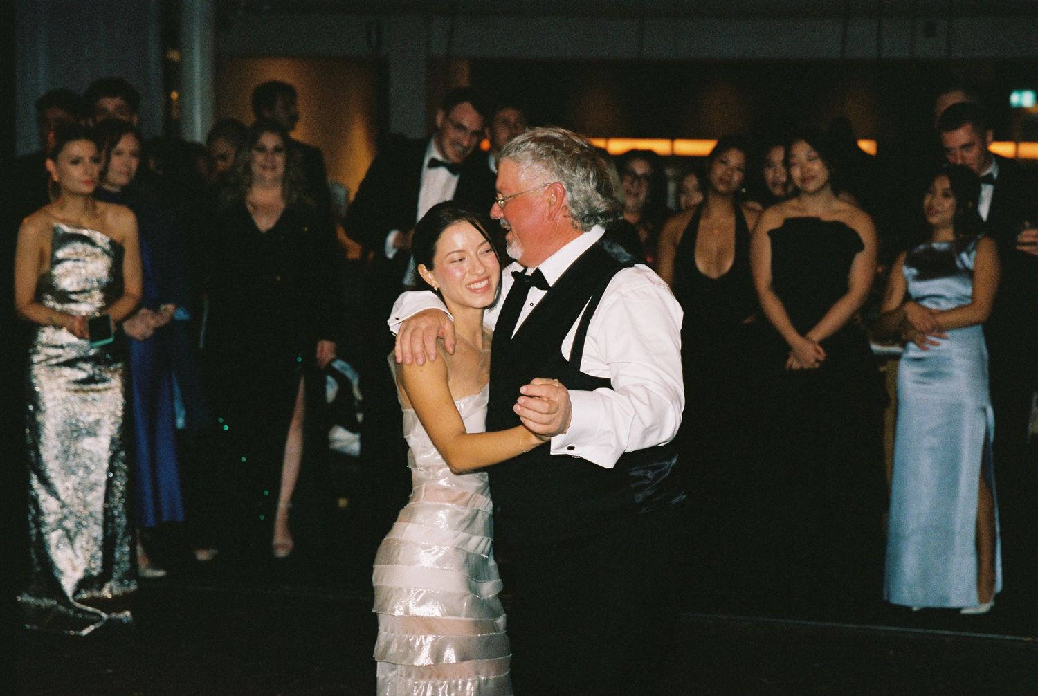 Bride and father share emotional first dance at wedding reception while guests watch.