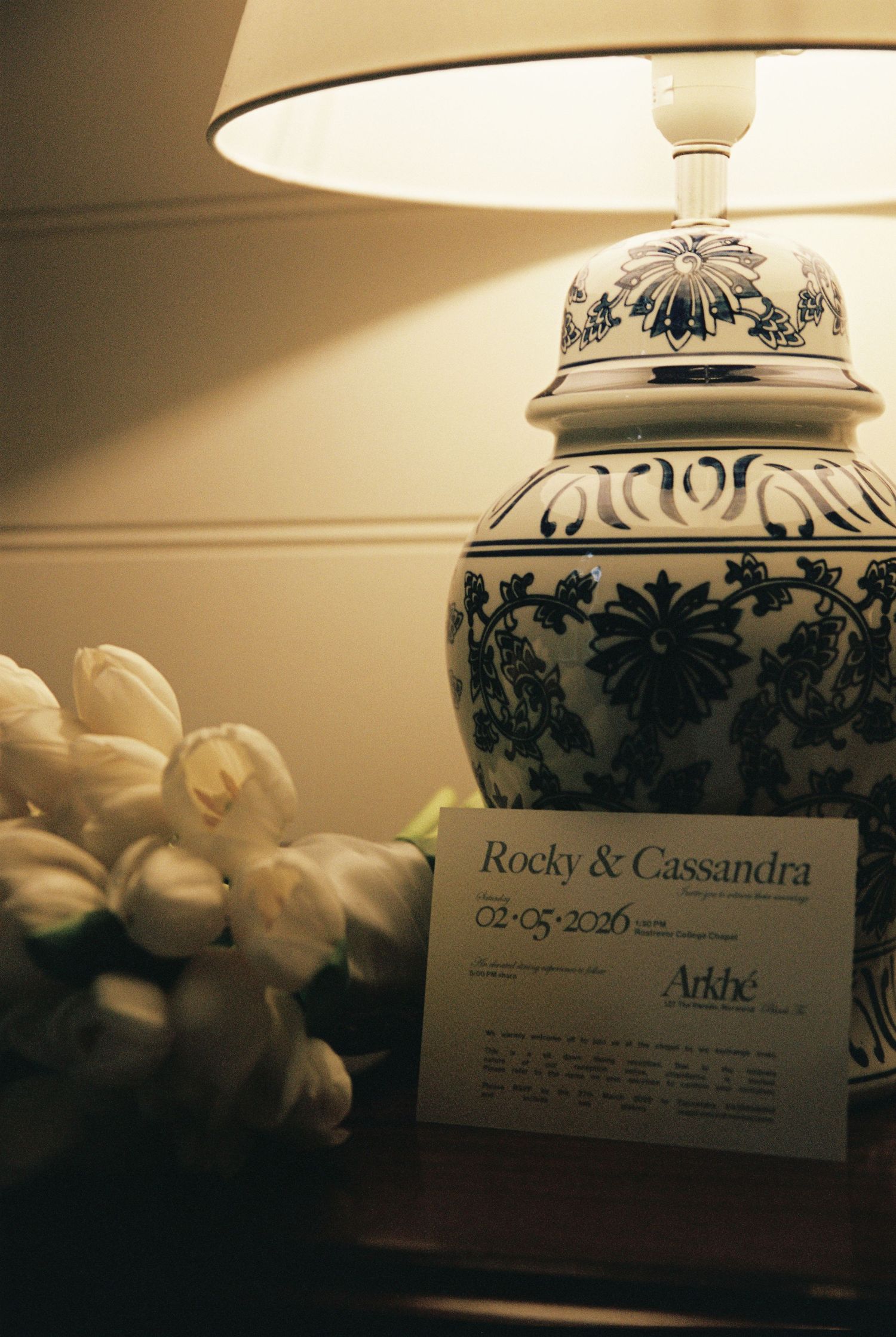 Elegant wedding invitation for Rocky and Cassandra beside a blue and white ginger jar lamp with tulips.