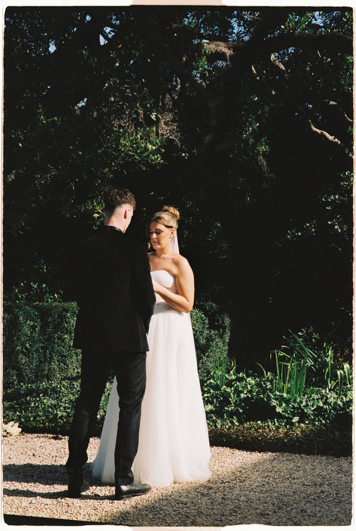 Bride in strapless white gown and groom in tuxedo share a tender garden ceremony moment.