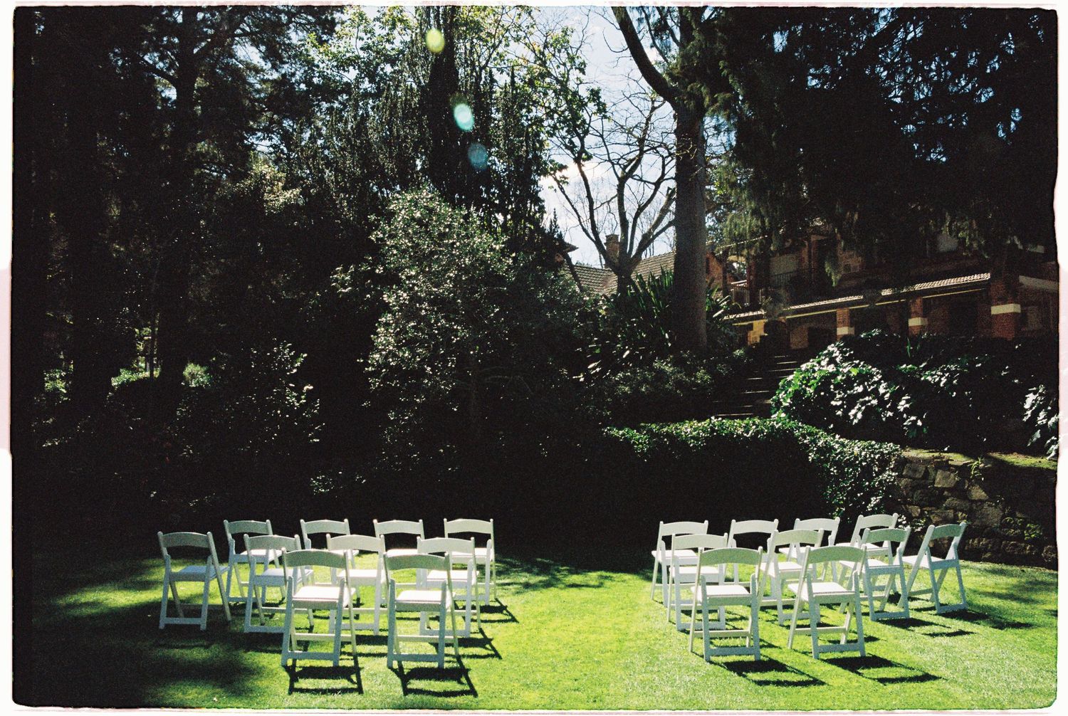 Empty white chairs arranged for an intimate outdoor garden wedding ceremony on a sunny lawn.