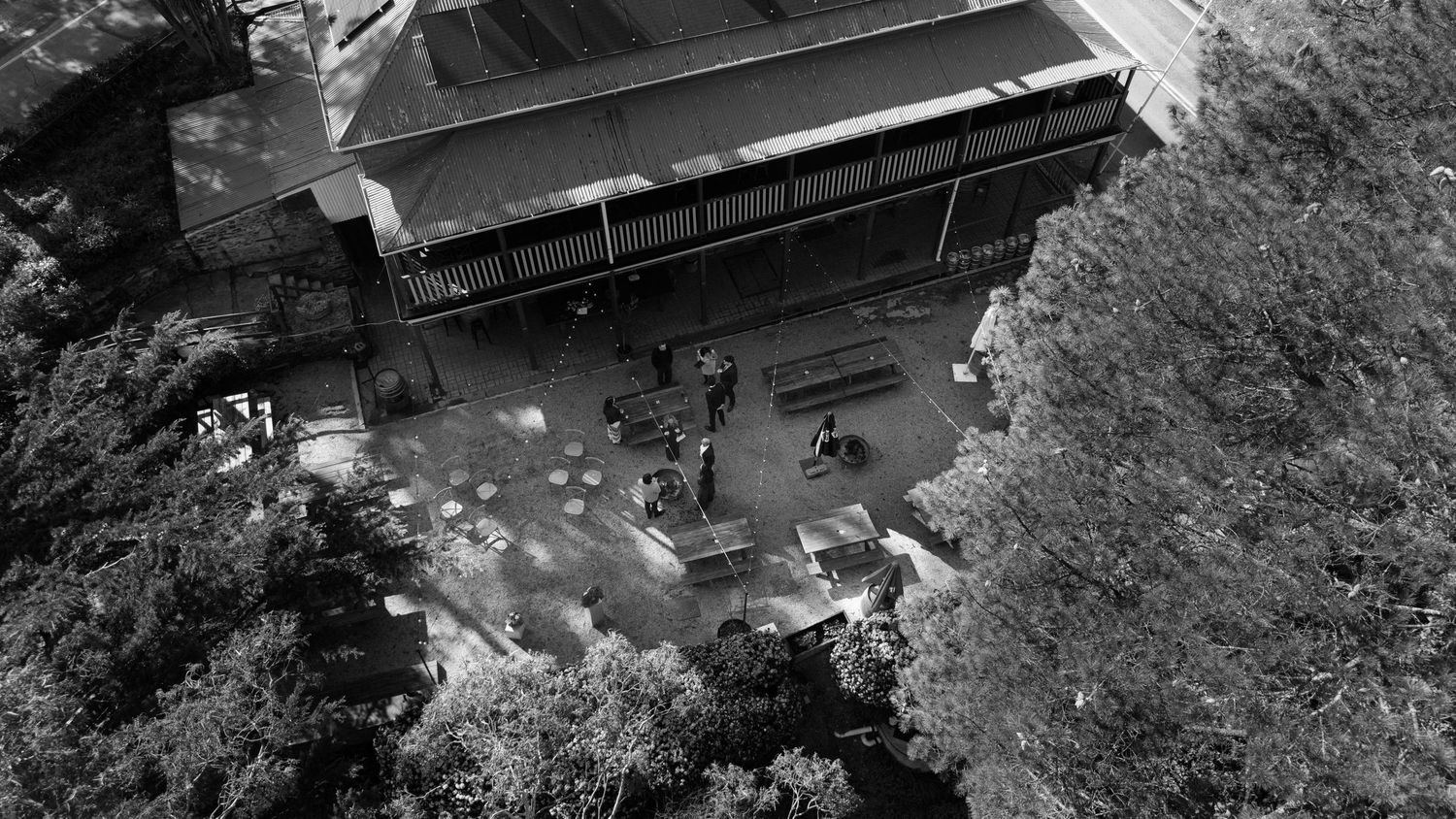 Aerial black and white view of a building surrounded by trees with people visible below.